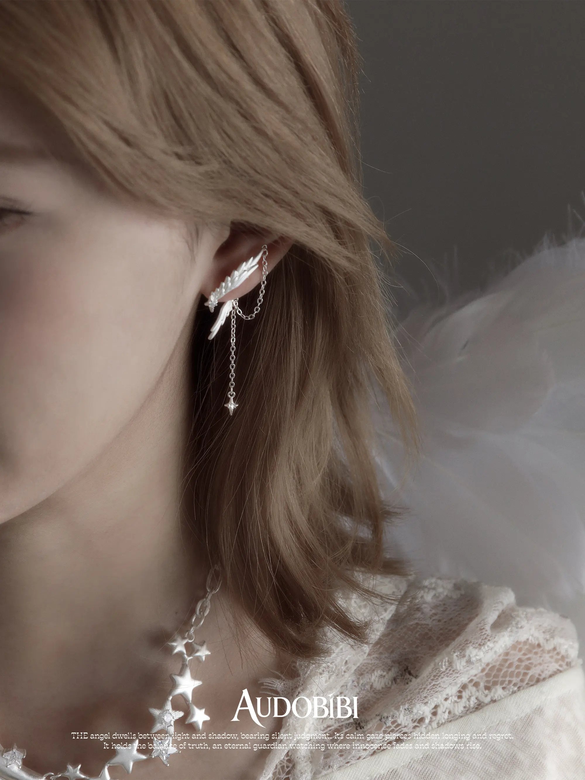 Asymmetric wing earrings with chain drops, shown in a close-up of the ear.