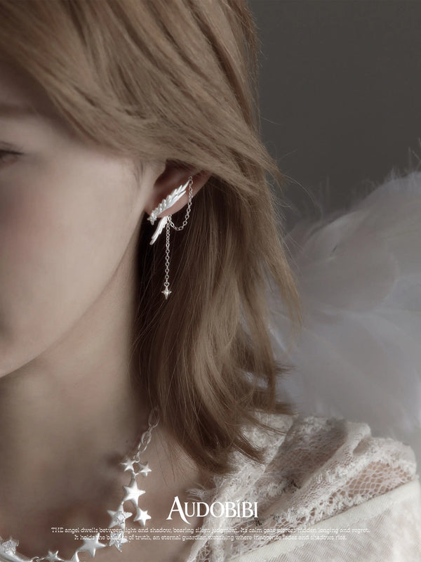 Asymmetric wing earrings with chain drops, shown in a close-up of the ear.