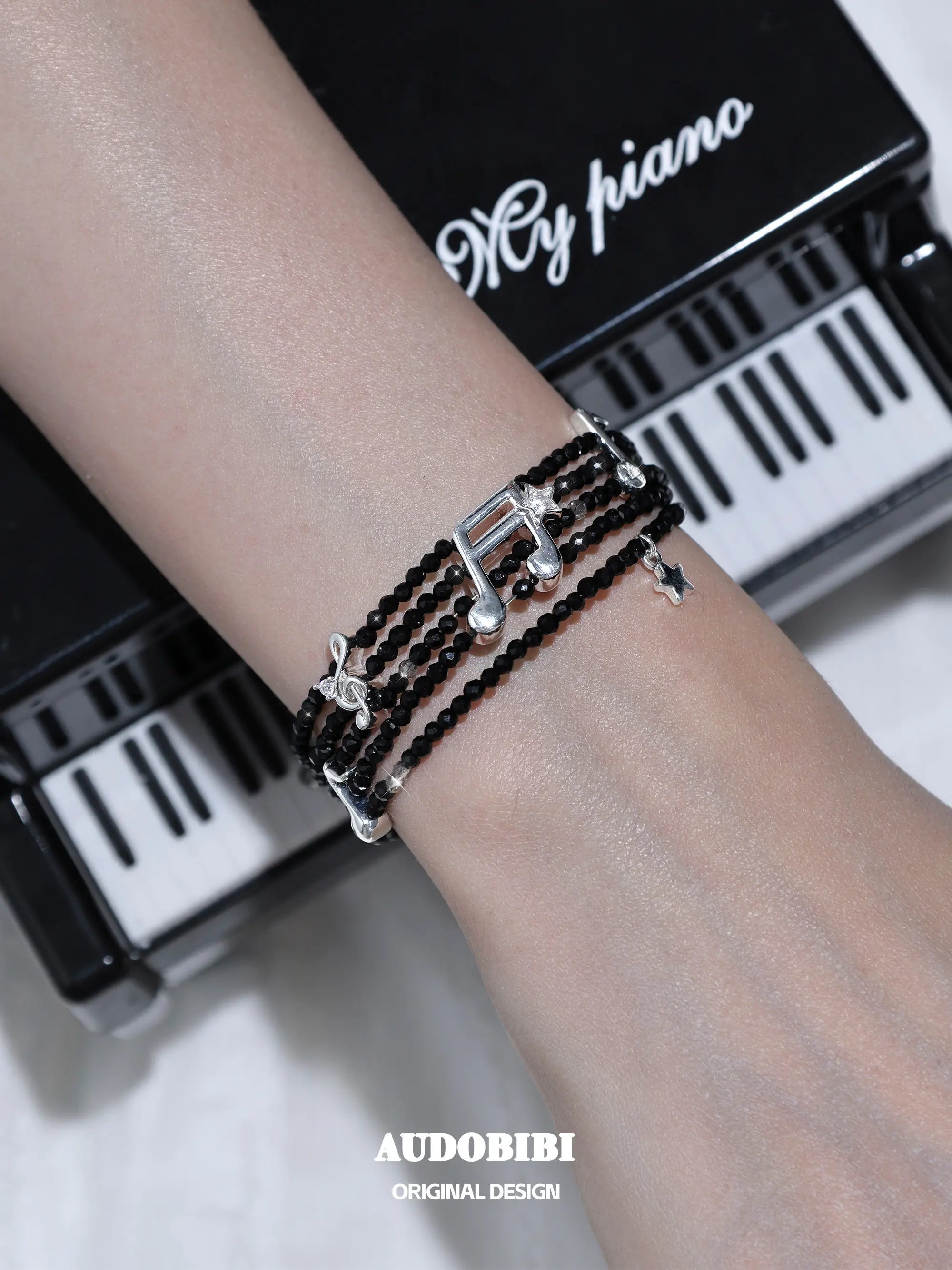 Black spinel musical-note bracelet, shown on the hand or wrist with other jewelry.