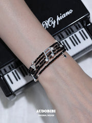 Black spinel musical-note bracelet, shown on the hand or wrist with other jewelry.