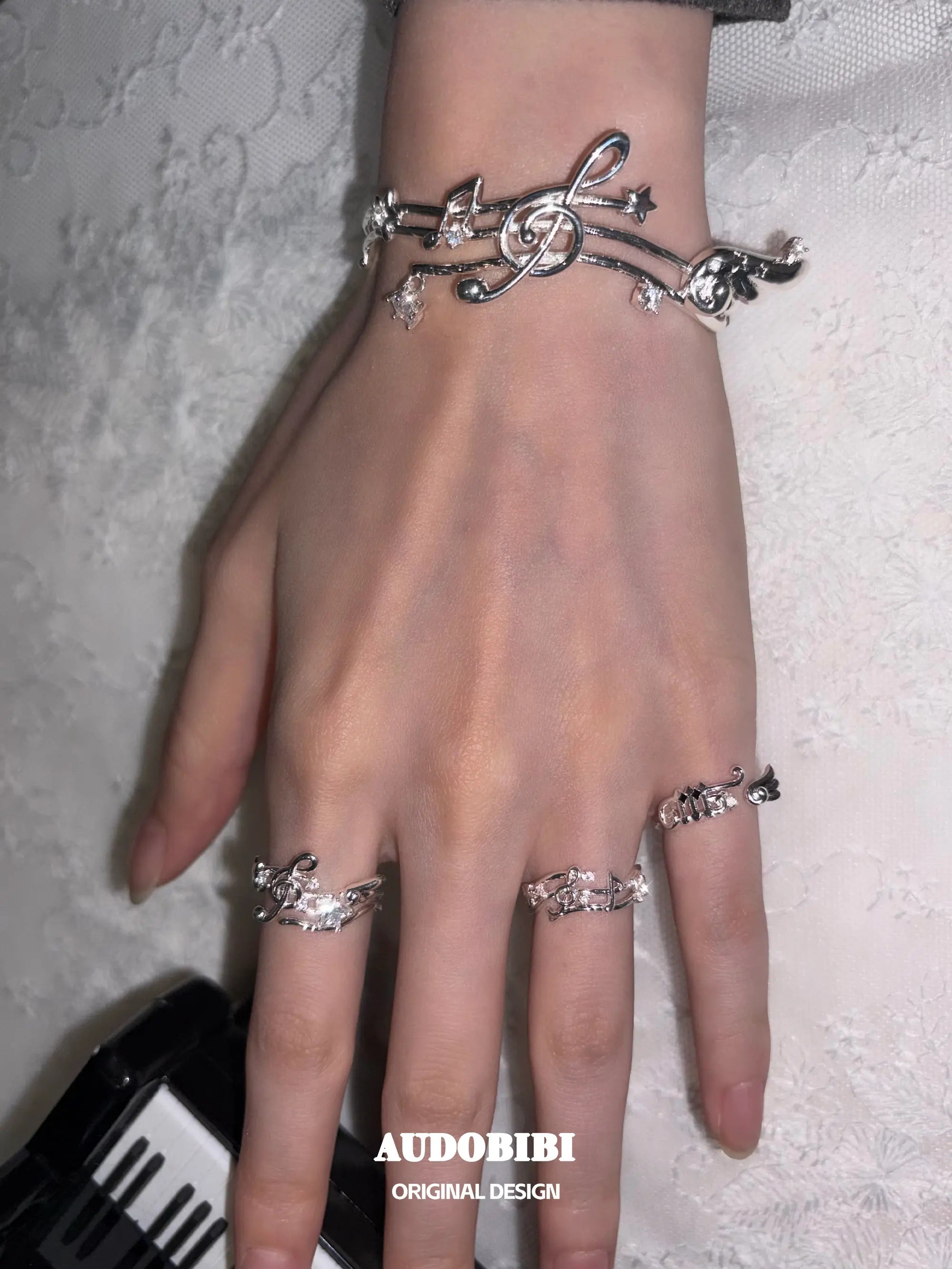 Musical-note pinky ring, shown on the hand or wrist with other jewelry.