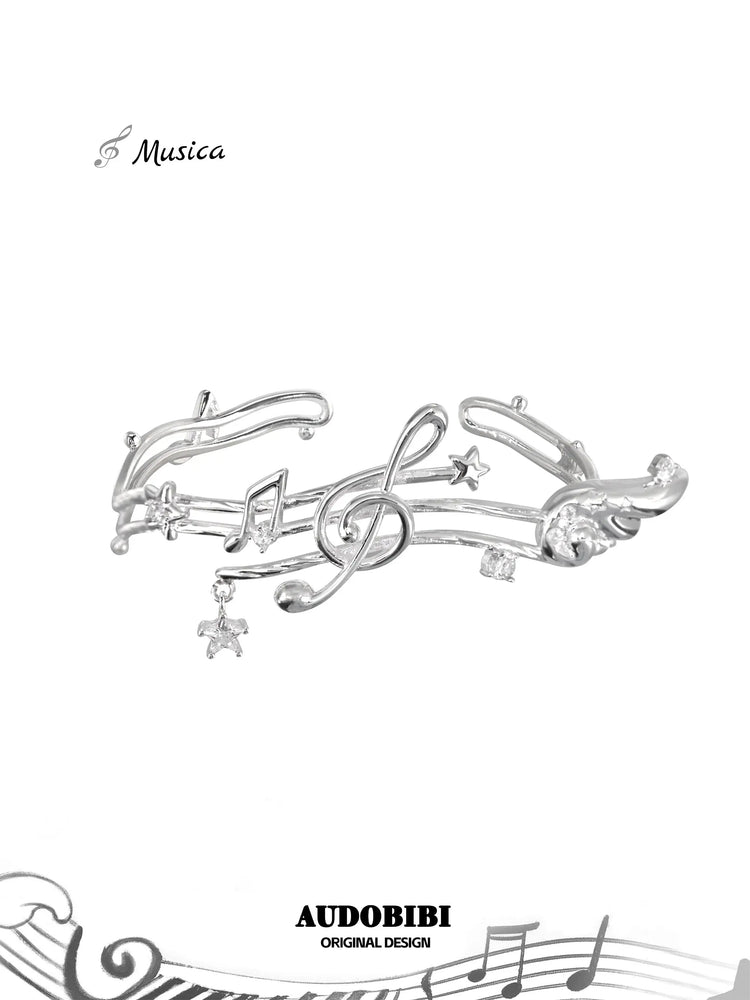 Open bangle shaped like a musical staff, with wing and hanging-star details.