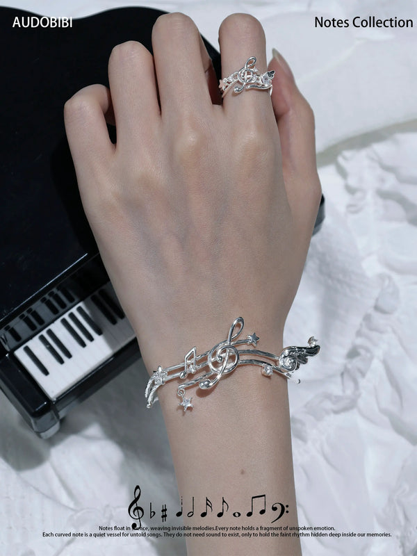 Musical-staff open bangle, shown on the hand or wrist with other jewelry.