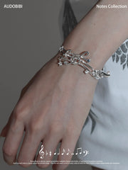 Musical-staff open bangle, shown on the hand or wrist with other jewelry.