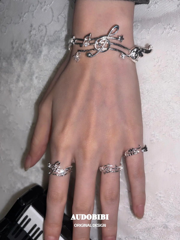 Musical-staff open bangle, shown on the hand or wrist with other jewelry.